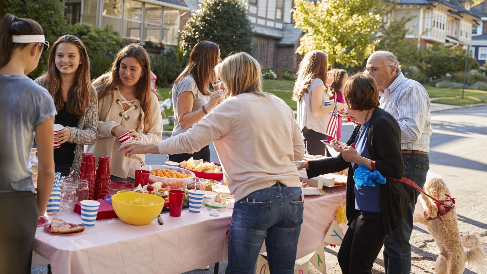 Junge und alte Nachbarn stehen an einem voll gepackten Tisch und feiern ein Fest.