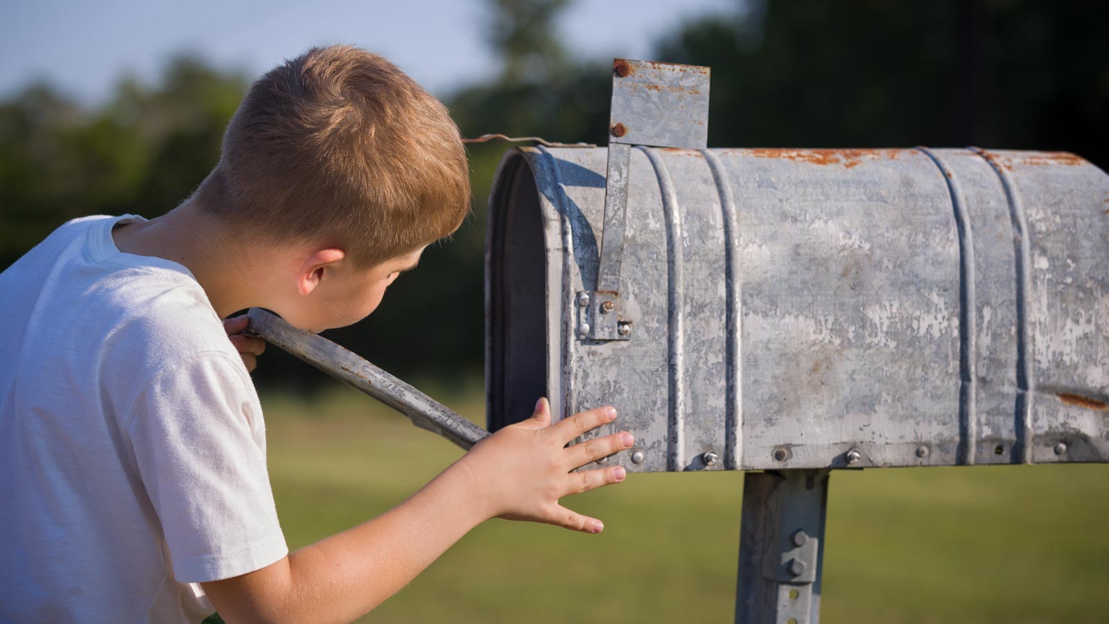 Junge schaut in einen Briefkasten.