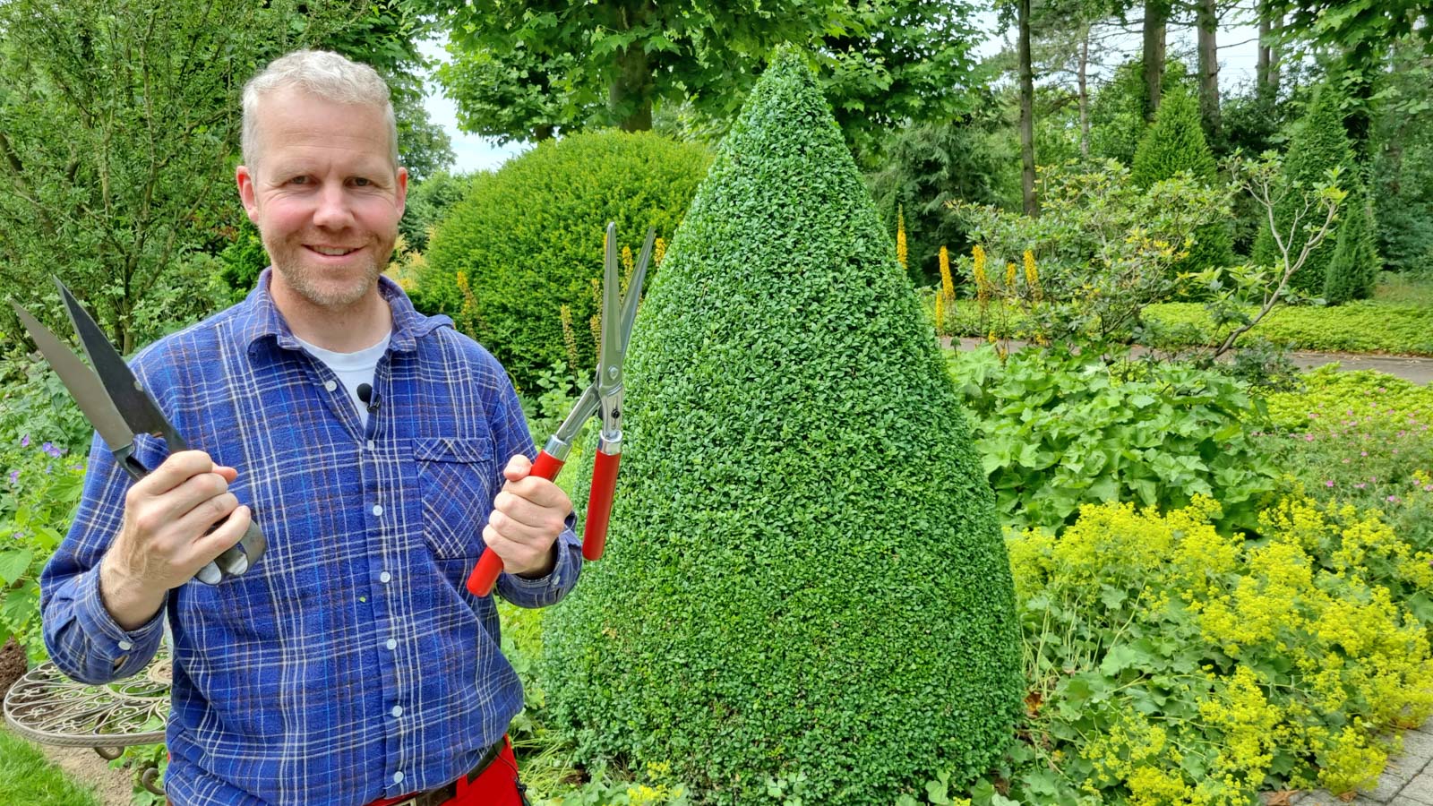 Gartenberater Philippe Dahlmann mit Schnittwerkzeug vor einem Buchsbaumkegel