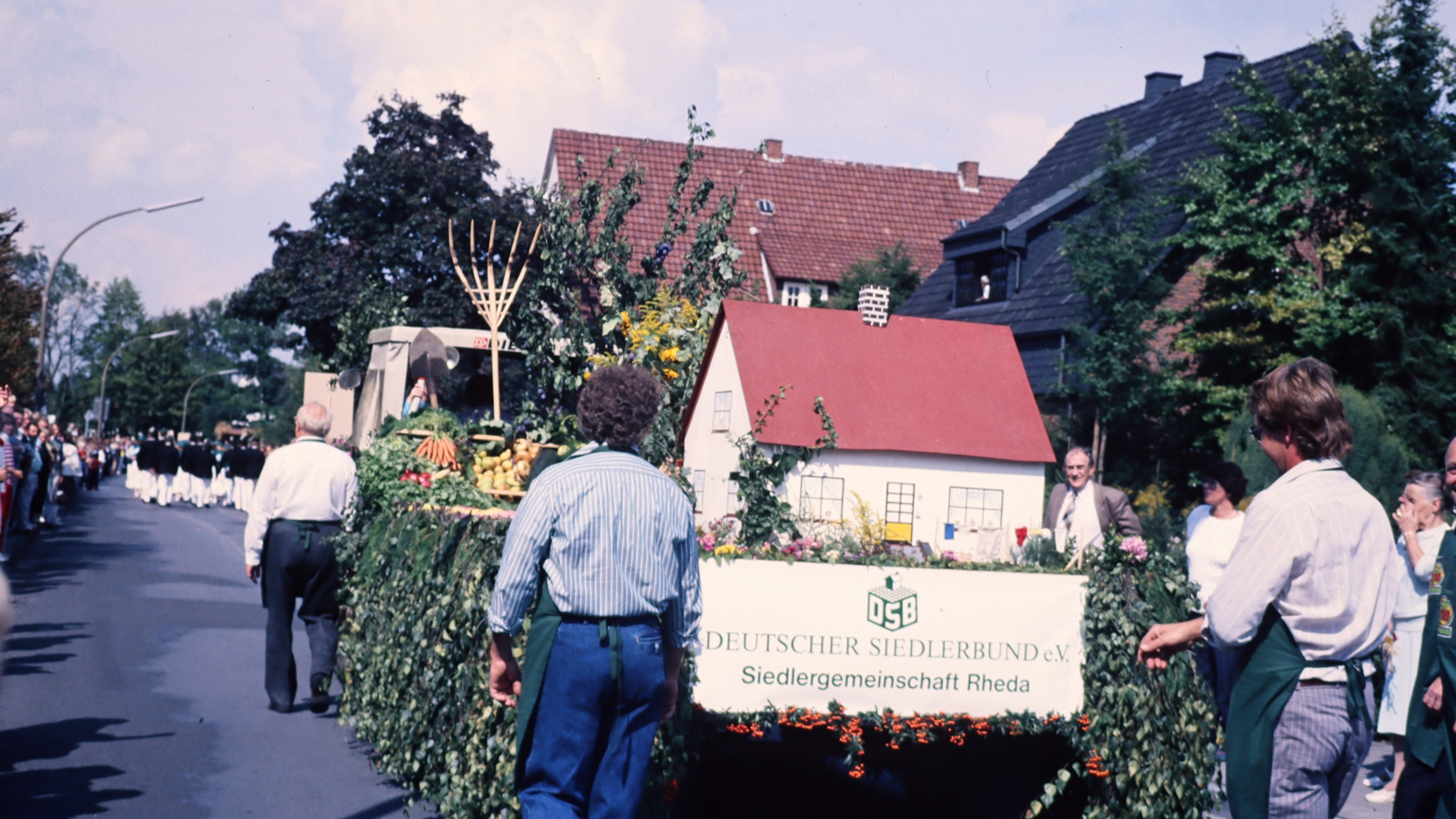Mitglieder der Gemeinschaft Rheda laufen bei einem Festumzug mit einem blumengeschmückten Wagen durch den Ort.