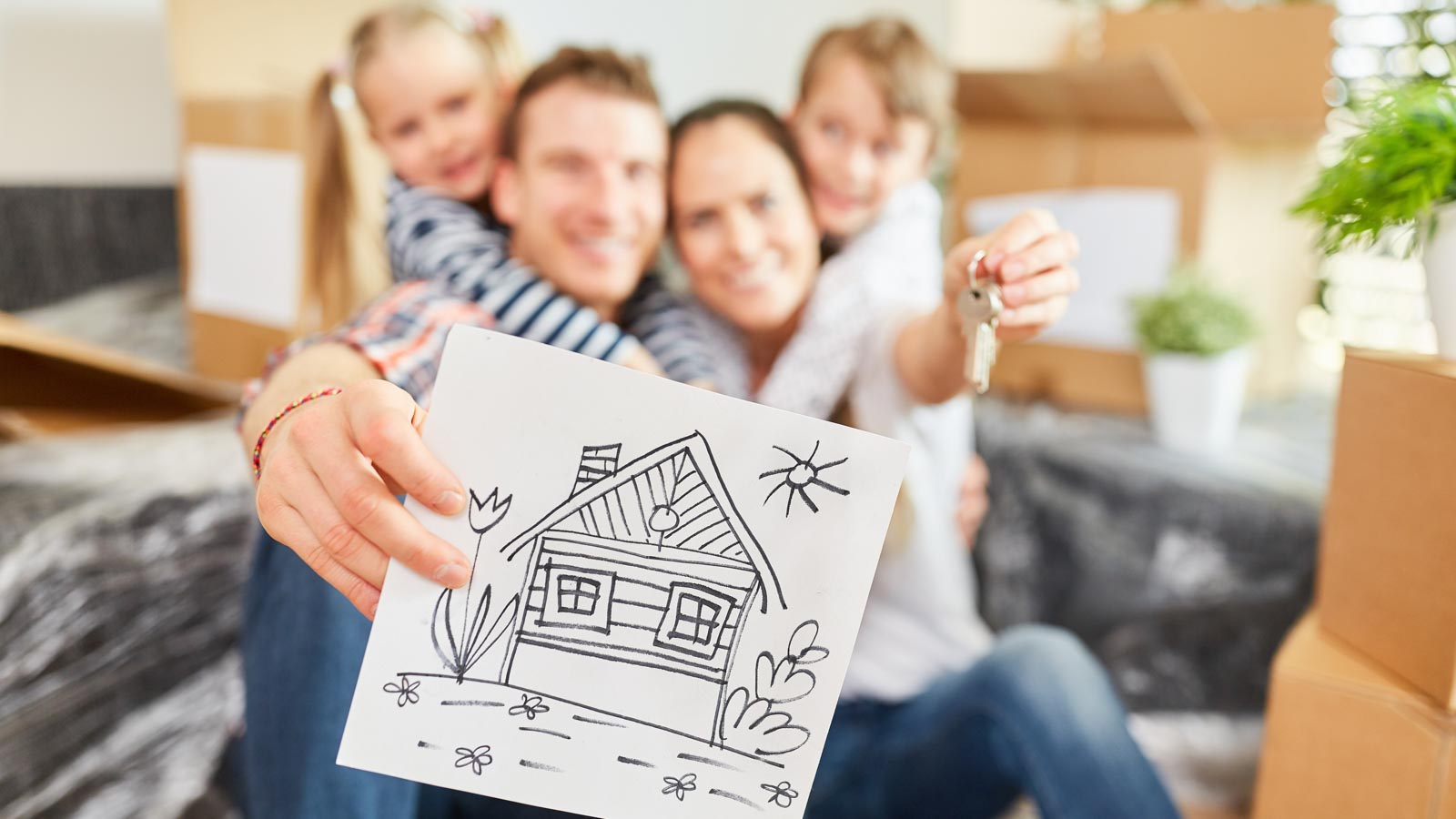 Familie mit zwei Kindern im Hintergrund unscharf hält eine Zeichnung von einem Haus zum Betrachter in den Vordergrund