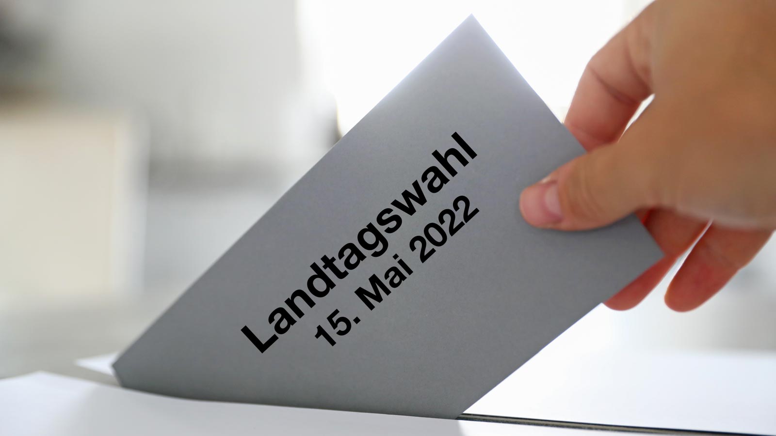 Hand wirft Umschlag mit der Aufschrift Landtagswahl 15. Mai 2022 in Wahlurne
