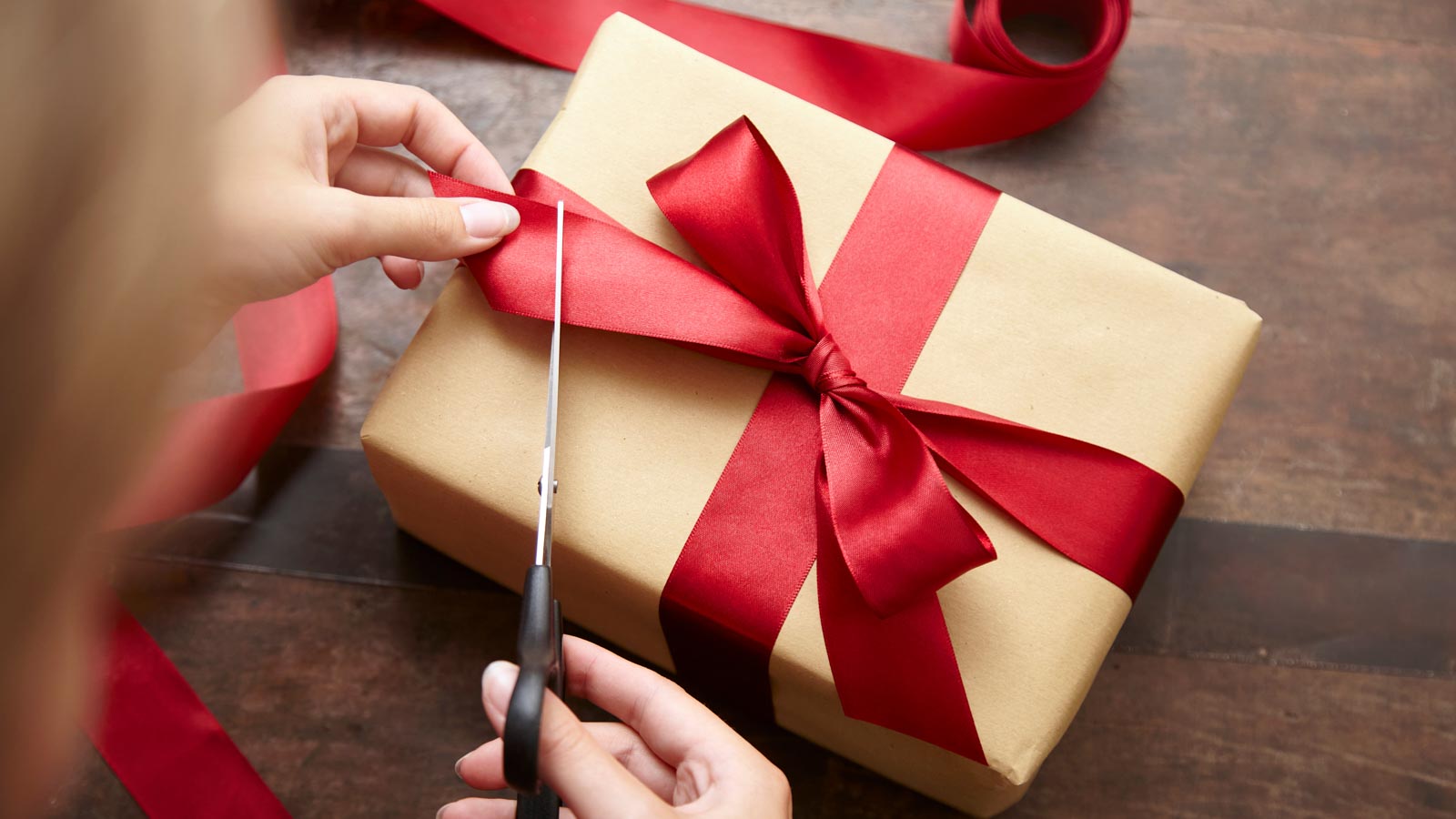 Frau schneidet das Schleifenband an einem Geschenk mit einer Schere ab