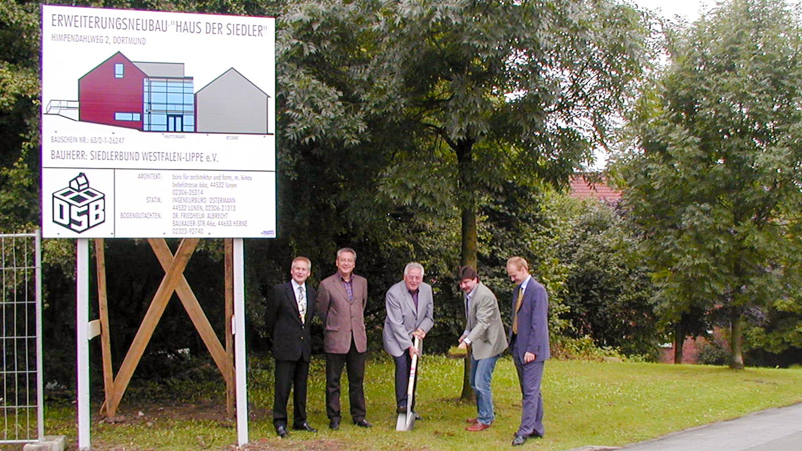 Personengruppe beim Spatenstich vor dem Bauschild für das neue Dienstgebäude