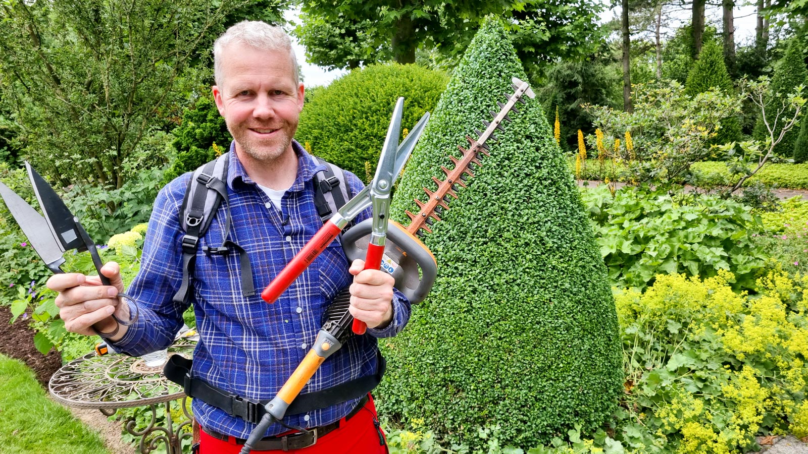 Gartenberater Philippe Dahlmann präsentiert Gartengeräte zum Buchsbaumschnitt vor einem geschnittenen Buchsbaum