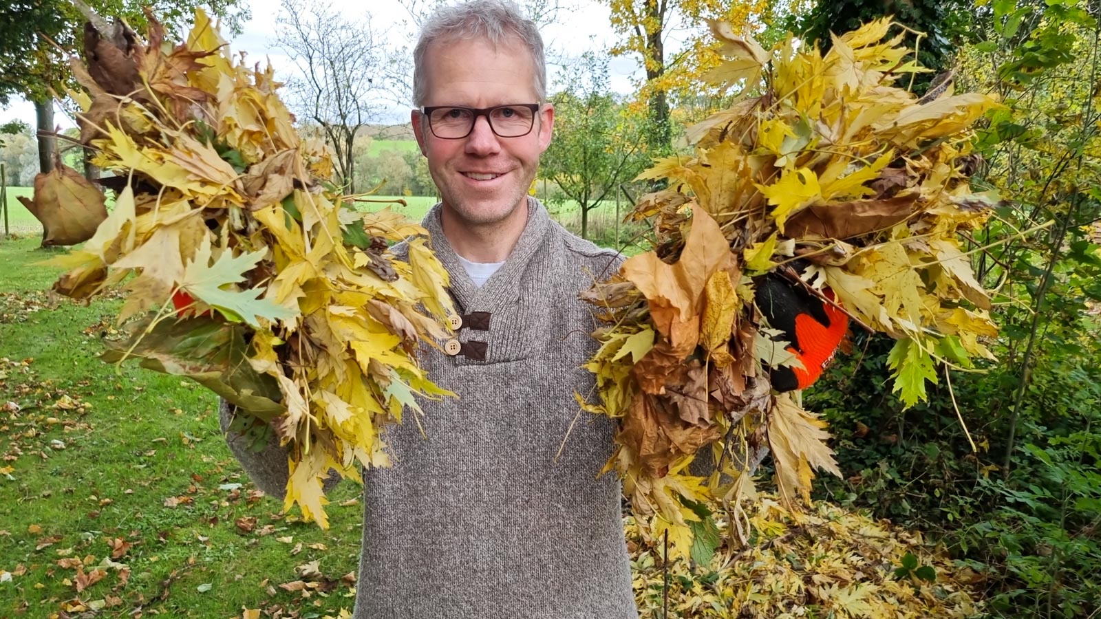 Halbtotale von Gartenberater Philippe Dahlmann, der mit beiden Händen Herbstlaub in Richtung Kamera hält