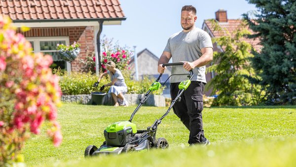 Mann mit Rasenmäher im Garten vor hübschem Einfamilienhaus