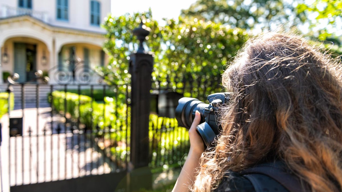 Frau fotografiert von außen ein Gebäude, das mit einem Zaun gesichert ist