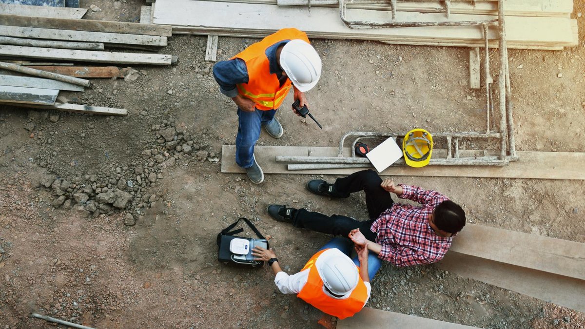 Zwei Bauarbeiter helfen einem Verletzten auf einer Baustelle
