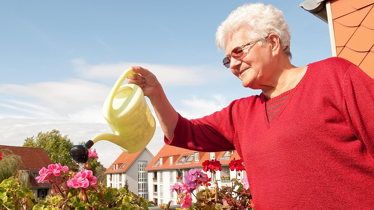 Ältere Frau gießt auf einem Balkon die Blumen