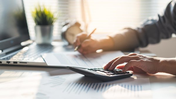 Laptop auf dem Tisch, Person mit Dokumenten und Taschenrechner