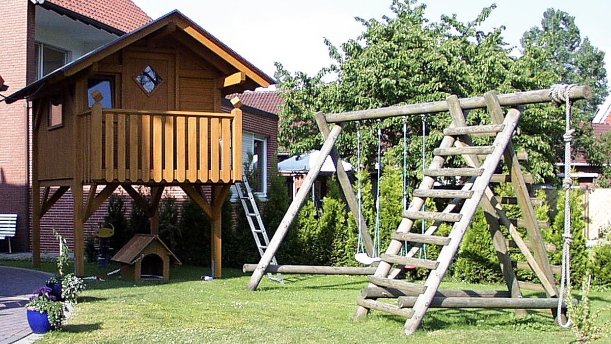 Kinder-Spielgerät mit Schaukel und Leiter und Holzhaus auf Stelzen im Garten