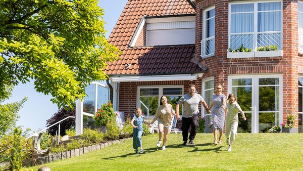 Fröhliche Familie im Garten vor Einfamilienhaus läuft auf die Kamera zu