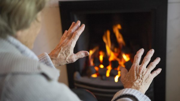 Ältere Frau von hinten, die vor einem Kamin sitzt und die Hände dorthin ausstreckt