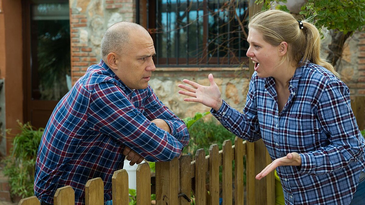 Nachbarn streiten sich am Gartenzaun, Frau gestikuliert mit den Händen