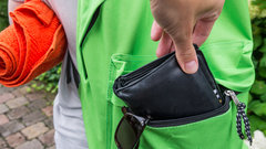 Taschendieb greift nach einem Portemonnaie aus einem grünen Rucksack
