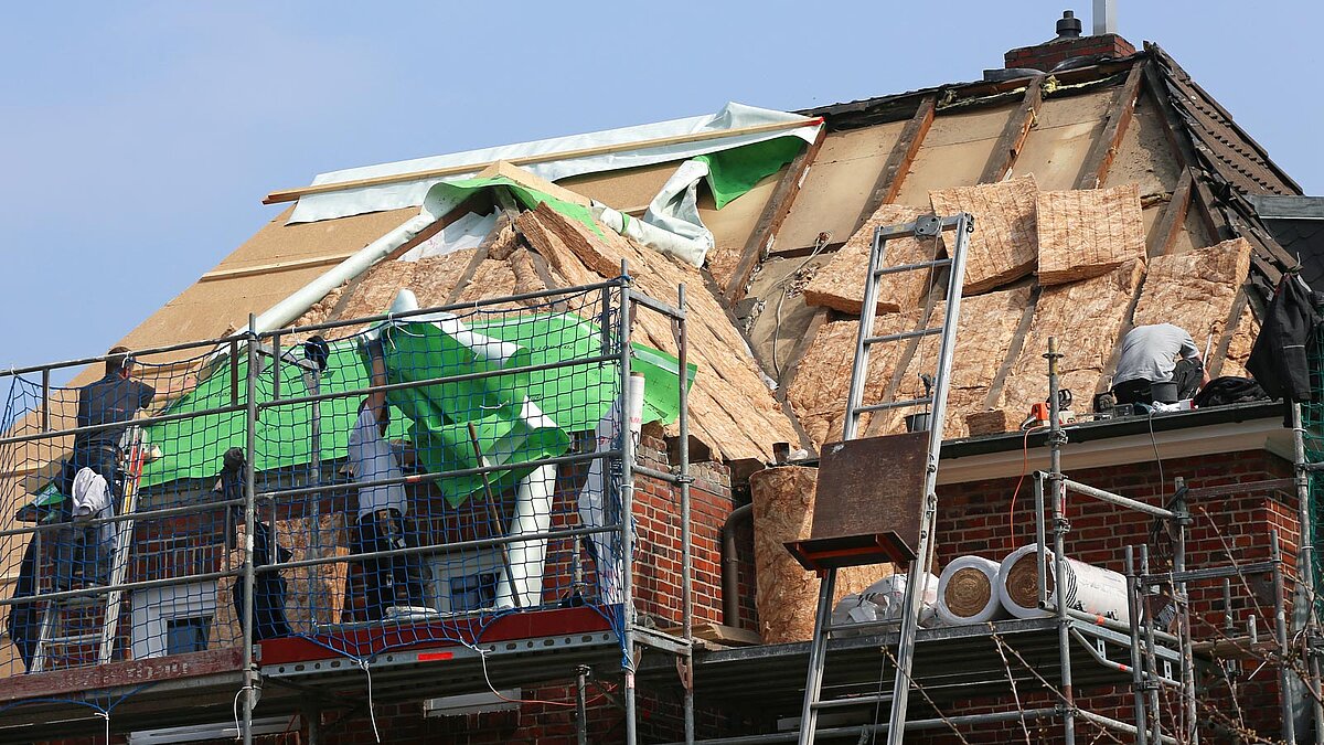 Handwerker auf einem Gerüst dämmen das Dach eines alten Hauses
