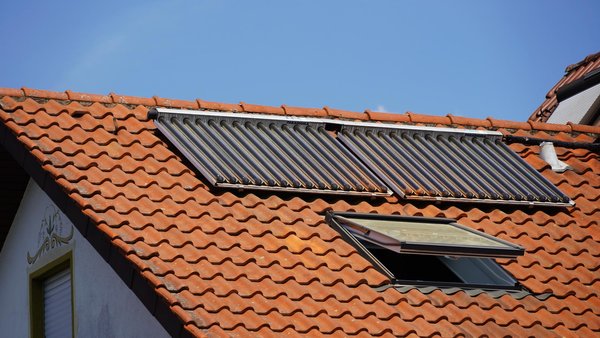 Solar Thermie Module auf einem Ziegeldach vor einem blauen Himmel.