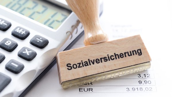 Stempel mit der Aufschrift Sozialversicherung neben Taschenrechner und Gehaltsabrechnung