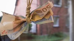 Herunterhängende Geldscheine am Galgen vor einem Wohnhaus.