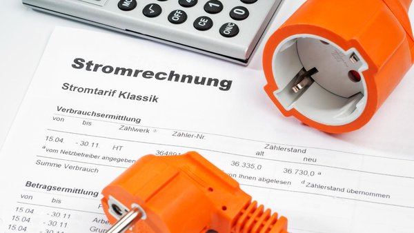 Stromrechnung, auf der ein Stecker und ein Taschenrechner liegen