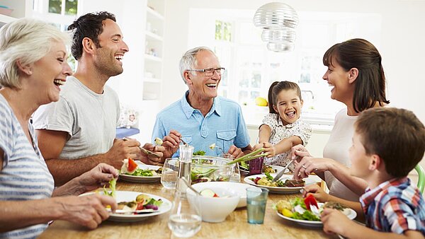 Familie mit mehreren Generationen sitzt lachend am Tisch und isst