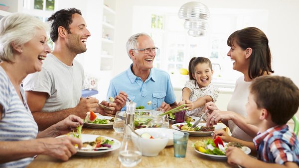 Familie mit mehreren Generationen sitzt lachend am Tisch und isst