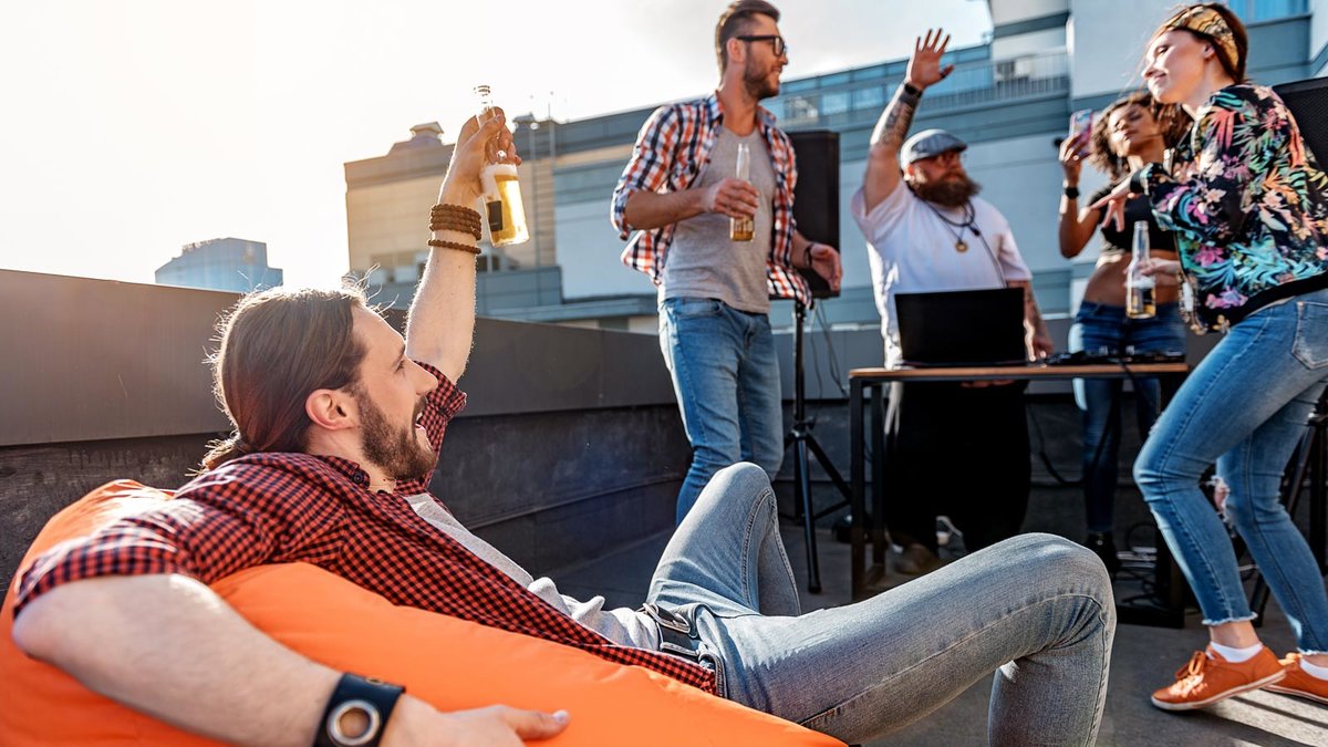 Gruppe junger Leute feiert mit Alkohol und Musik auf einem Balkon