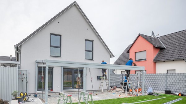 Terrasse hinter einem Haus wird von Handwerkern überdacht