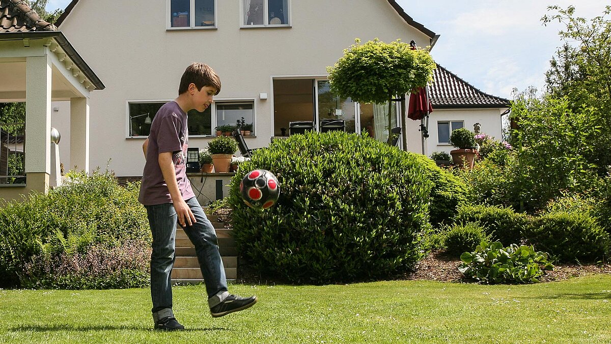 Junge spielt im Garten eines Hauses alleine Fußball
