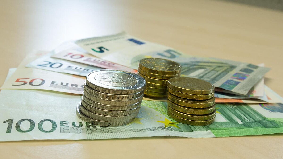 Gefächerte Geldscheine und Stapel von Euromünzen