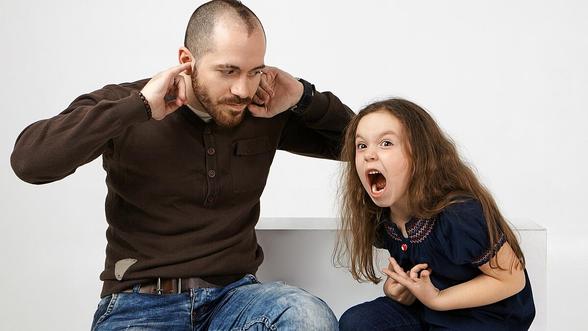Schreiendes Mädchen neben ihrem Vater, der sich die Ohren zuhält