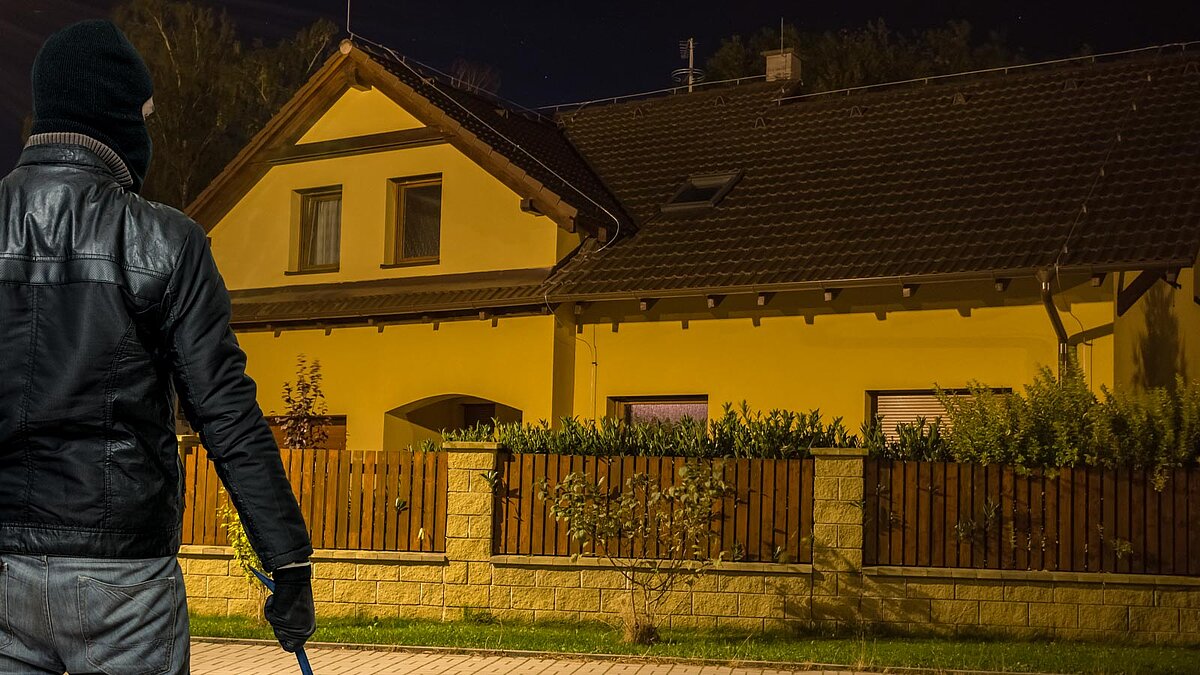Vermummter Einbrecher steht nachts vor einem Haus
