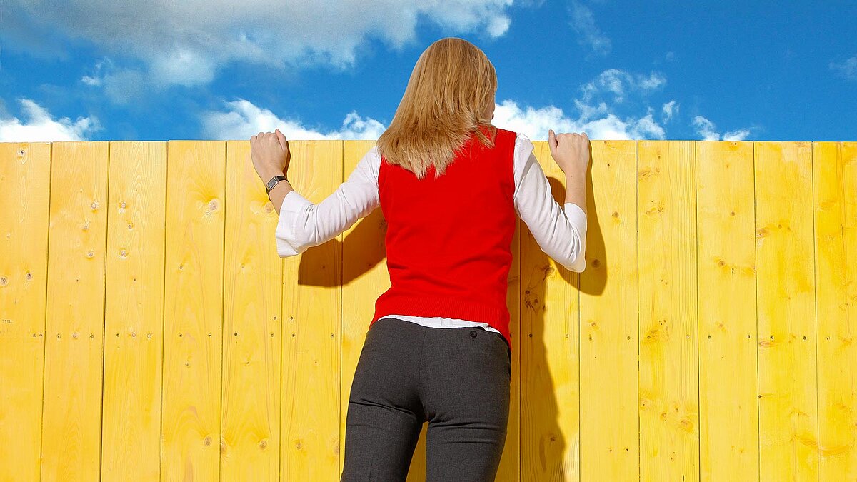 Von hinten abgebildete Frau schaut über einen Zaun