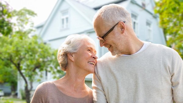 Älteres Paar steht vor einem Haus und lächelt sich an
