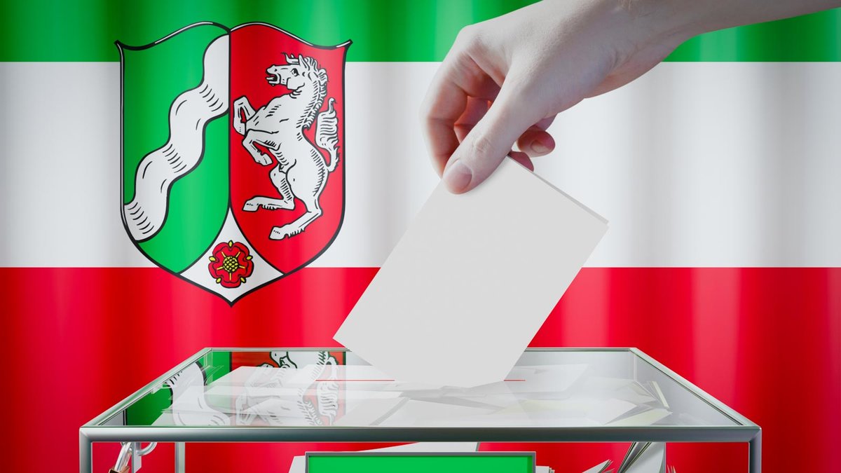 Hand wirft Wahlzettel in Urne, im Hintergrund NRW-Flagge