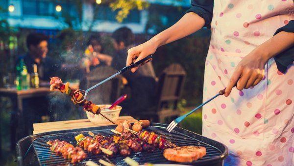 Im Vordergrund Frau am Grill vor Personen, die abends an einem Tisch sitzen