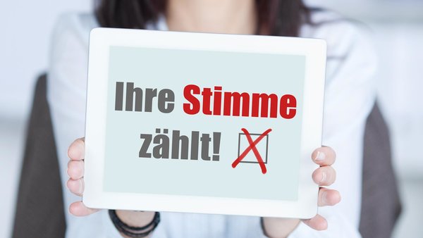 Eine Frau hält ein Schild in ihren Händen auf dem steht "Ihre Stimme zählt"