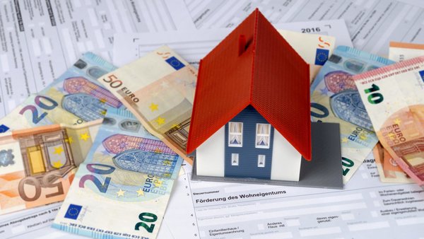 Modellhaus auf gefächerten Euroscheinen und Antrag zur Förderung des Wohneigentums