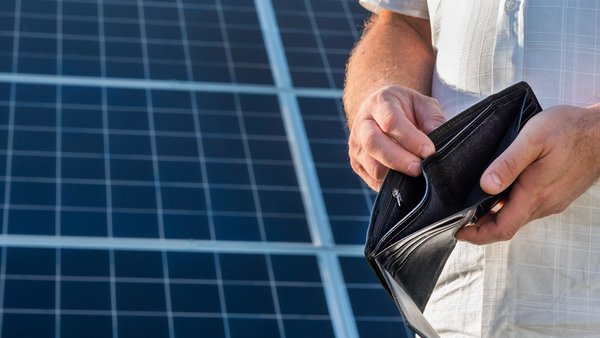 Mann mit einem leeren GEldbeutel, auf dem Dach eines Hauses, mit Solaranlage