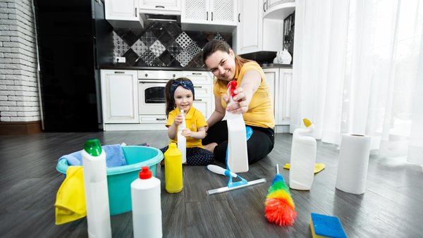 Mutter und Kind mit Putzmitteln kniend vor eine Küche