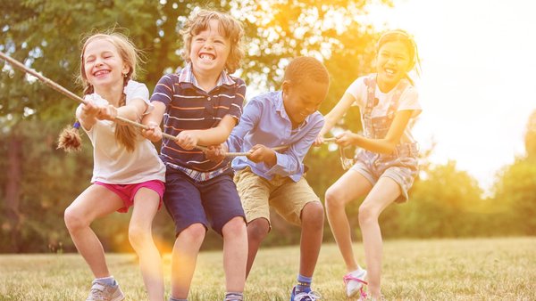 Fröhliche Mädchen und Jungen spielen Tauziehen im Garten. 