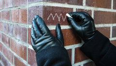 Behandschuhte Hand malt Kreidezeichen auf Hauswand