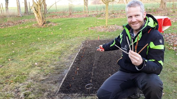 Gartenberater Philippe Dahlmann kniend vor einem Steckholz Beet mit Steckhölzern in der Hand