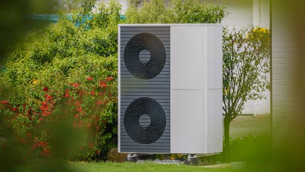 Die Außeneinheit einer Wärmepumpe steht vor einem Haus in einem Garten