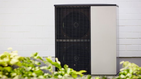 Eine Wärmepumpe steht in einem begrünten Vorgarten vor einem Haus