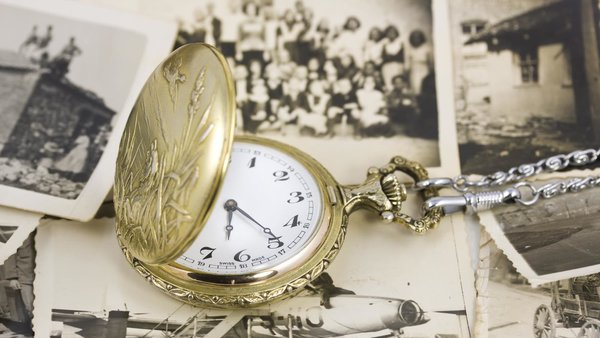 Eine goldene Taschenuhr liegt auf einem Stapel antiker Fotos.