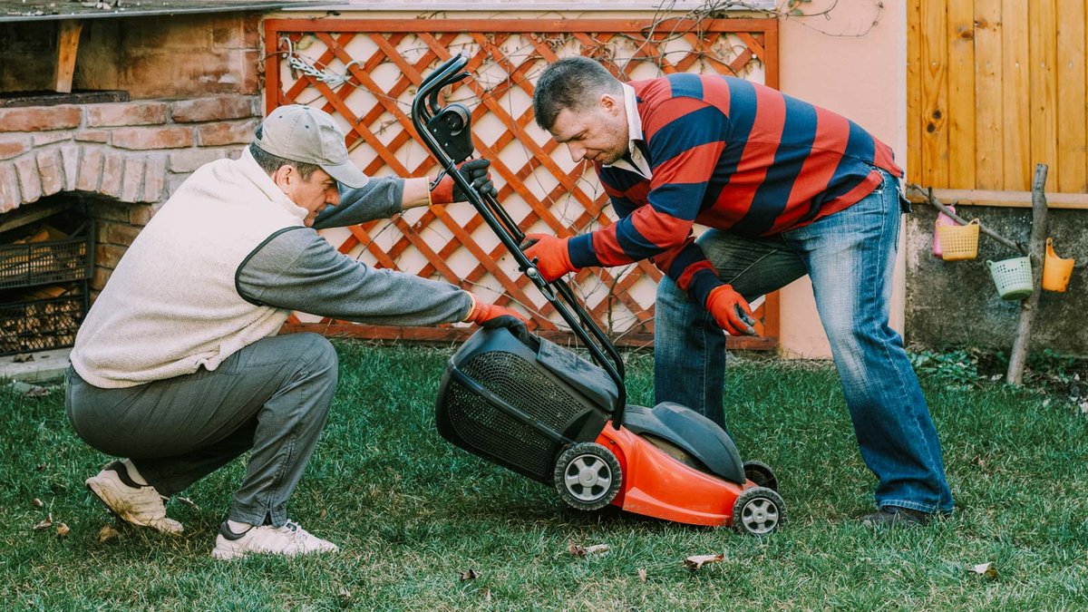 Zwei Personen reinigen einen Rasenmäher 