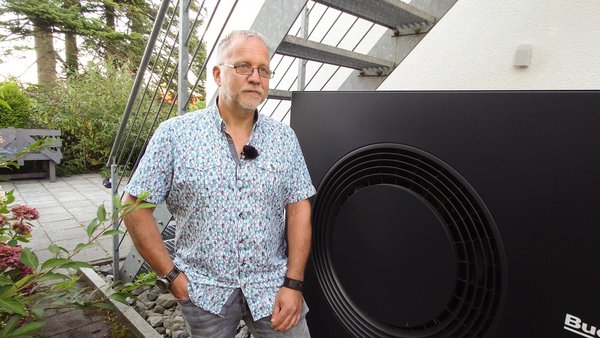 Ein Mann steht vor einem Haus an einem Außengerät einer Wärmepumpe. 