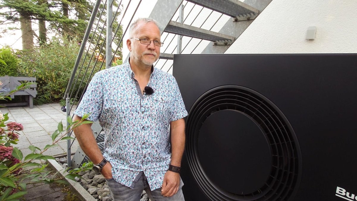 Ein Mann steht vor einem Haus an einem Außengerät einer Wärmepumpe. 